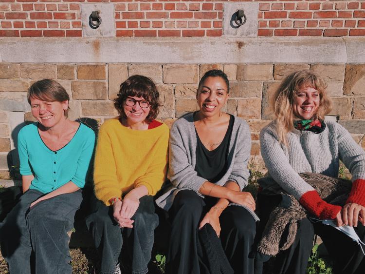 4 femmes assises sur la bordure d'un trottoir au soleil