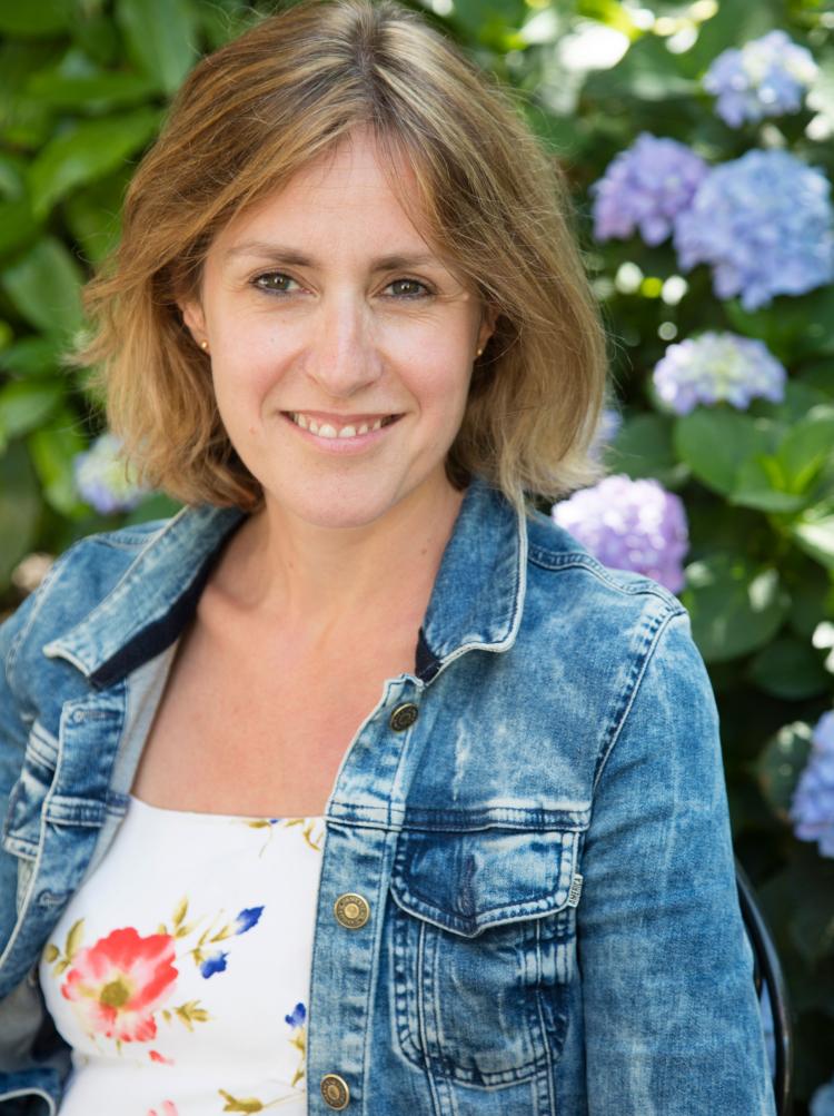 femme souriante avce une veste en jeans devant des hortensias