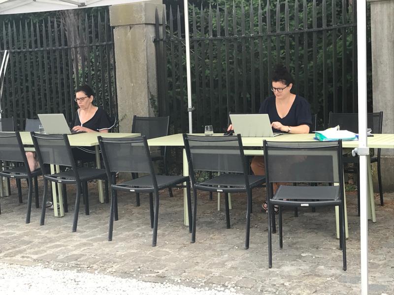 2 femmes assises sur des tables sous une tonnelle devant leur ordinateur