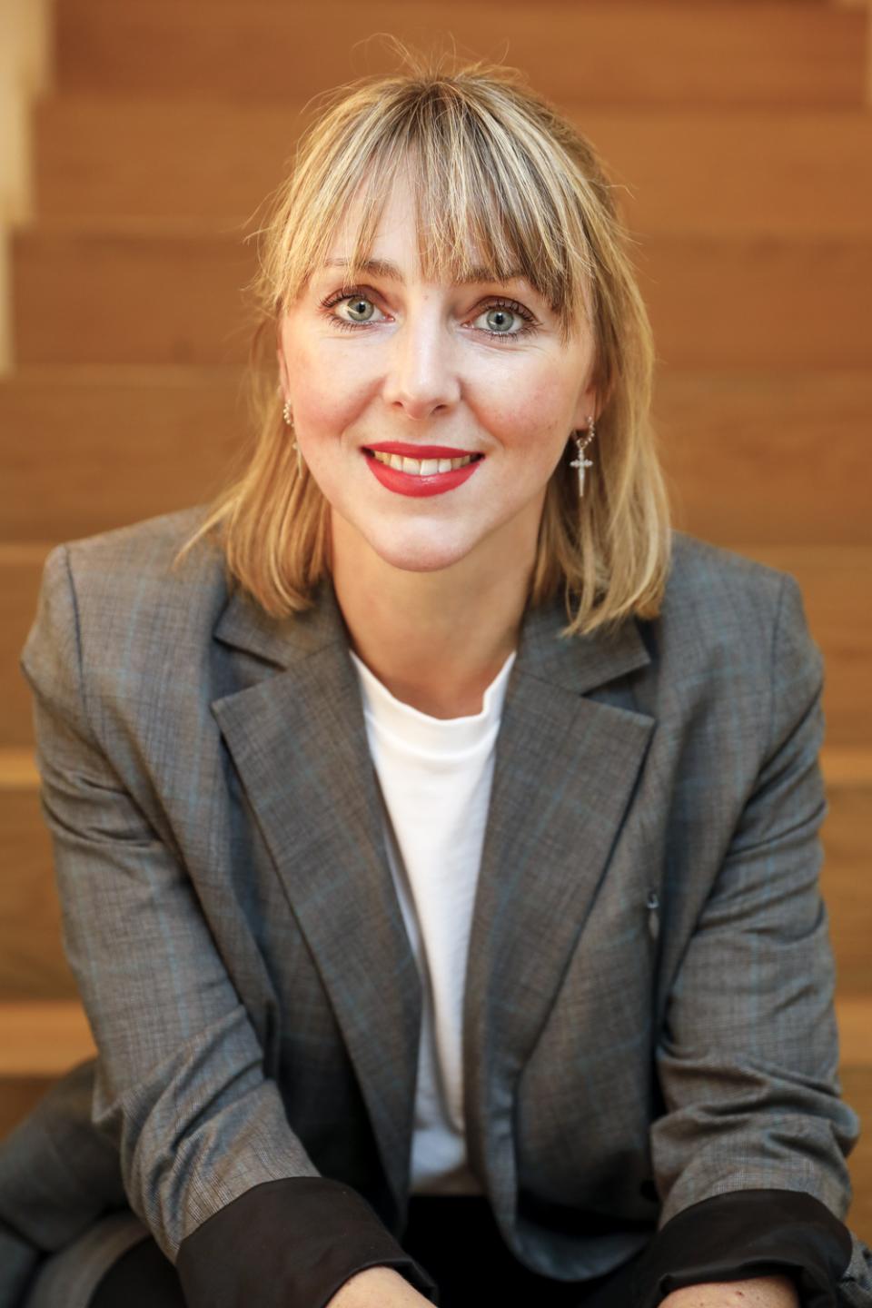 femme blonde avec rouge à lèvres rouge et blaiser gris assise sur des escaliers