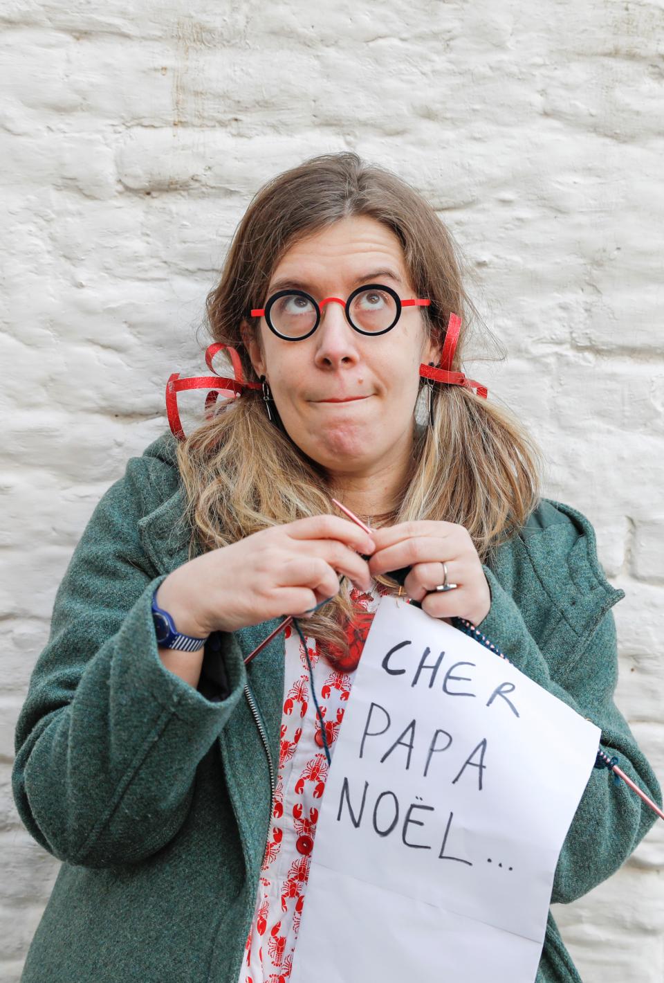 femme avec lunettes tricotant une lettre et levant les yeux au ciel